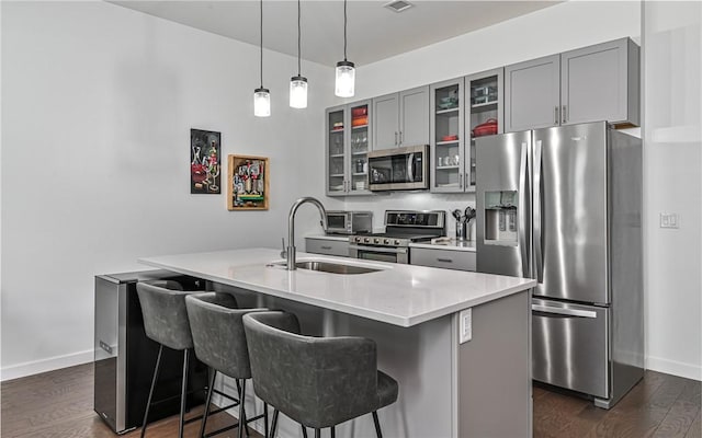 kitchen featuring stainless steel appliances, a sink, gray cabinetry, dark wood-type flooring, and a breakfast bar area