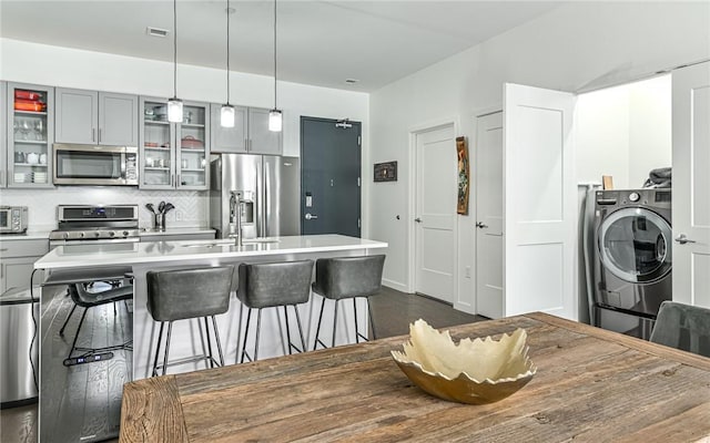 kitchen featuring a sink, a breakfast bar area, stainless steel appliances, washer / clothes dryer, and gray cabinetry