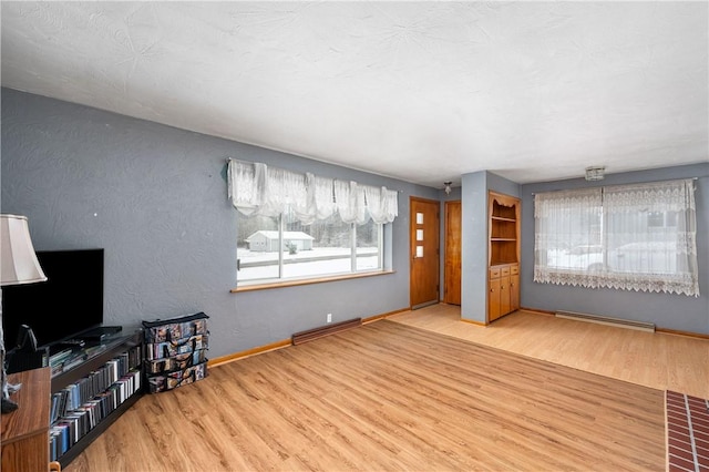 unfurnished living room with a baseboard heating unit, baseboards, wood finished floors, and visible vents