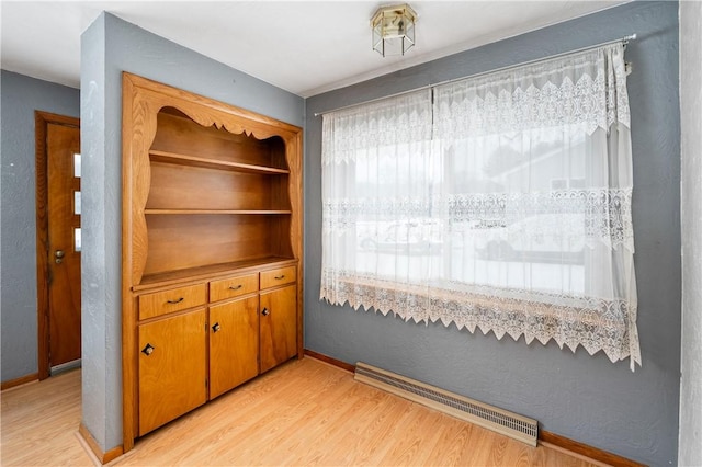 interior space with a baseboard radiator, baseboards, and light wood-type flooring