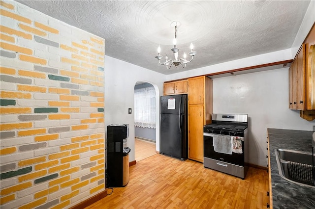 kitchen featuring stainless steel range with gas cooktop, a textured ceiling, arched walkways, freestanding refrigerator, and light wood-style floors