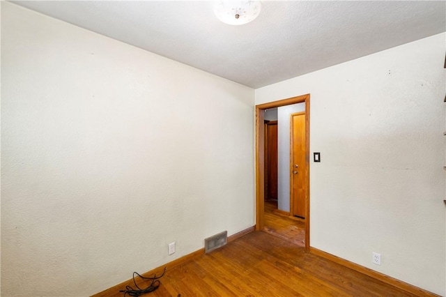 empty room with wood finished floors, visible vents, and baseboards