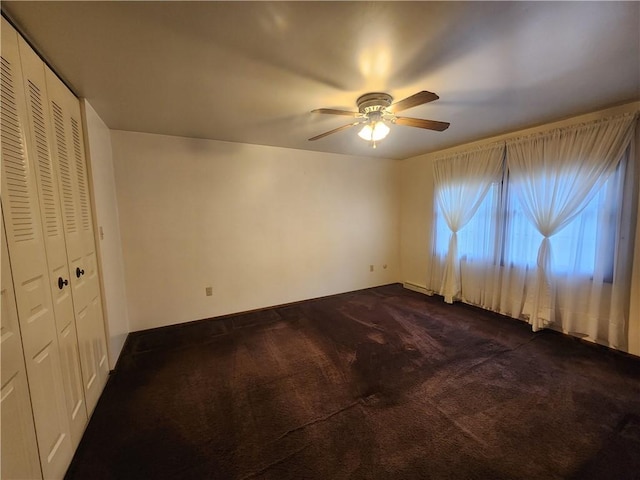 unfurnished bedroom with a ceiling fan, a closet, dark colored carpet, and baseboards