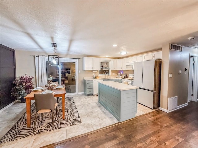 kitchen with white cabinets, a sink, visible vents, light countertops, and white appliances