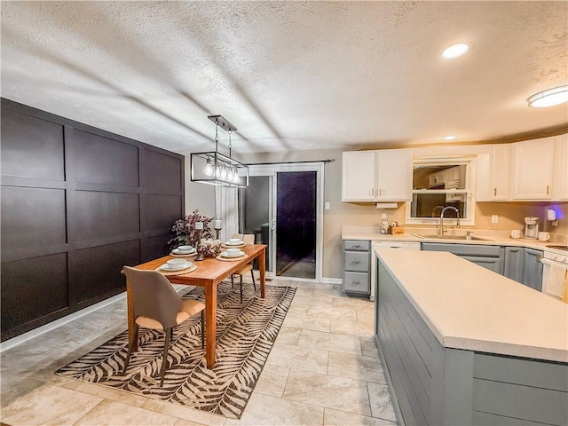 kitchen featuring gray cabinetry, light countertops, white cabinets, and a sink