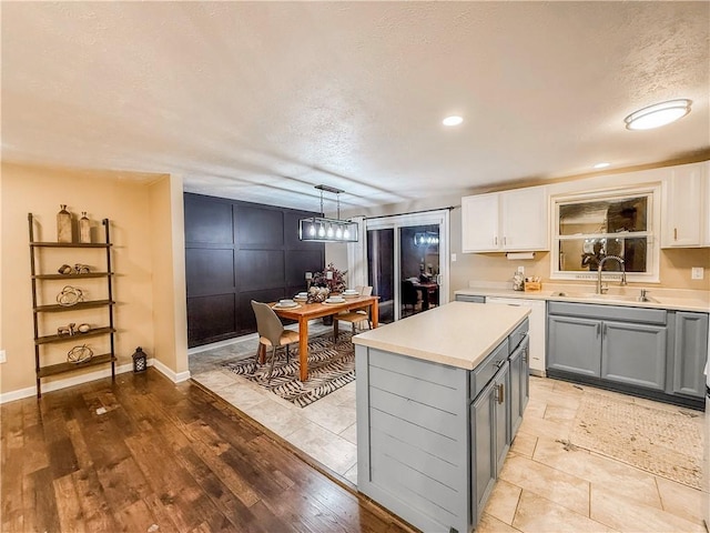 kitchen featuring a kitchen island, light countertops, a sink, gray cabinetry, and a textured ceiling