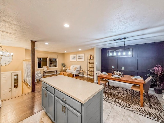 kitchen with a notable chandelier, a kitchen island, light countertops, gray cabinetry, and hanging light fixtures