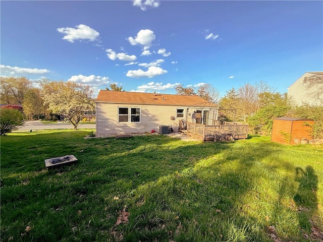 back of house featuring a deck, an outdoor structure, a yard, central air condition unit, and a shed