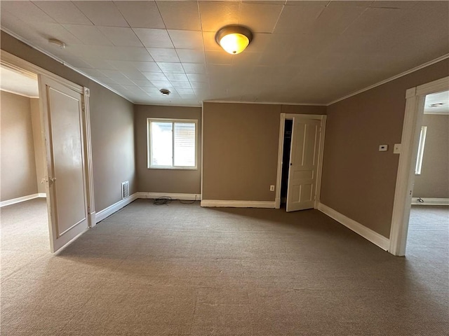 carpeted empty room with visible vents, crown molding, and baseboards