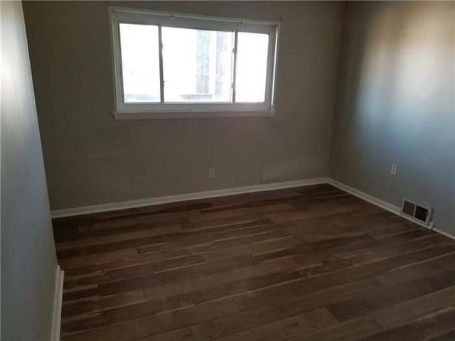 spare room with visible vents, baseboards, and dark wood-type flooring