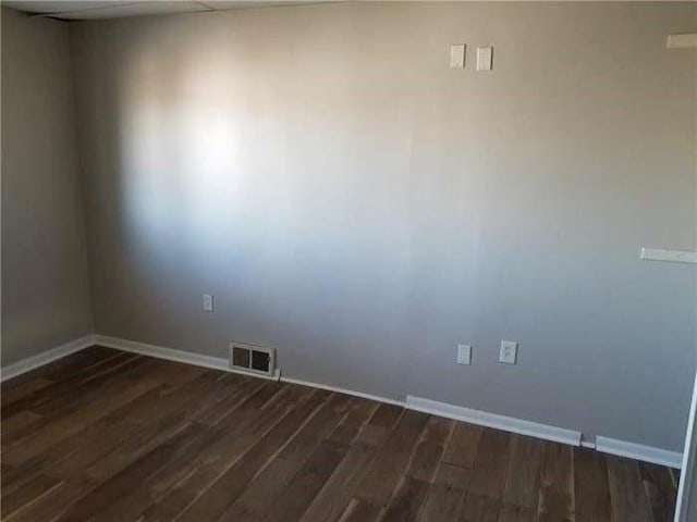unfurnished room featuring dark wood-style flooring, visible vents, and baseboards