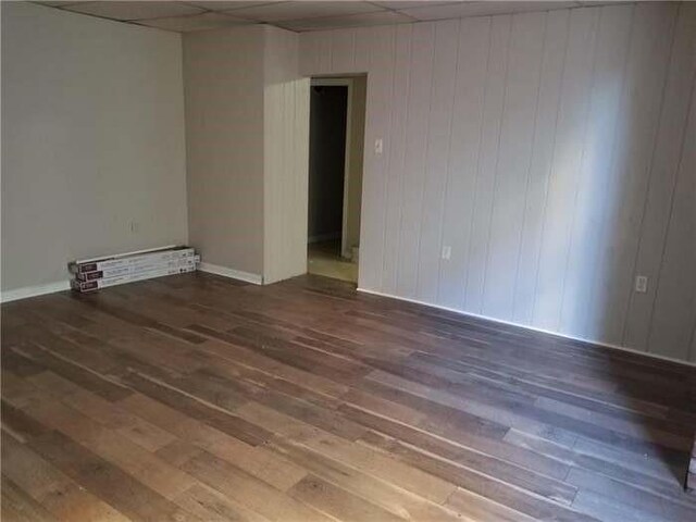 empty room with a drop ceiling, wood finished floors, and baseboards