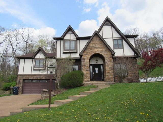 tudor home featuring concrete driveway, a front yard, an attached garage, stucco siding, and brick siding