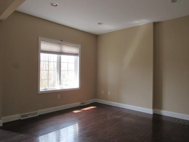 spare room with visible vents, baseboards, and dark wood finished floors