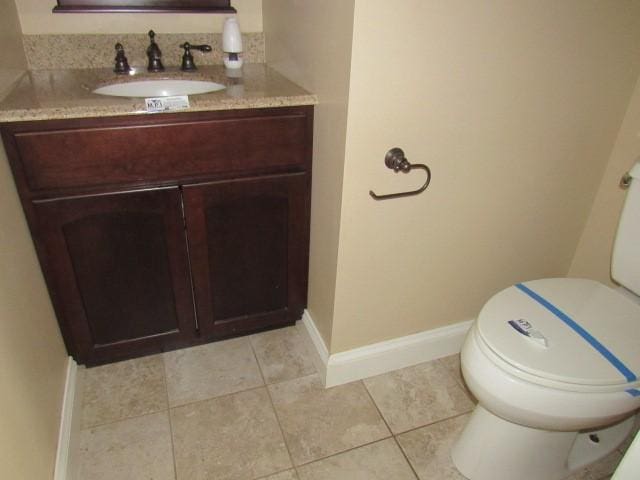 half bathroom with toilet, tile patterned floors, vanity, and baseboards