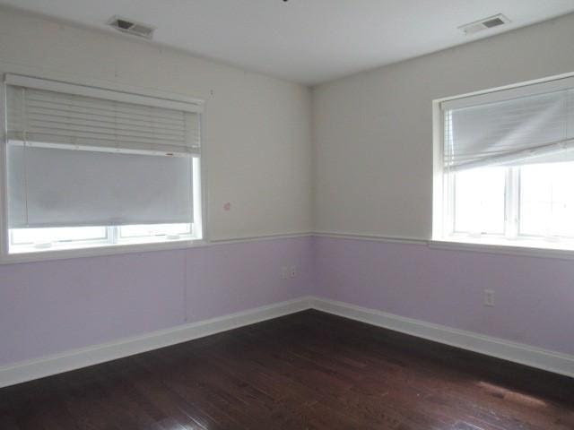unfurnished room featuring visible vents, hardwood / wood-style floors, and baseboards