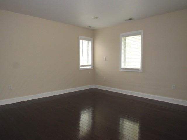 unfurnished room with dark wood-type flooring, visible vents, and baseboards