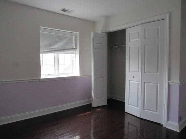 unfurnished bedroom featuring wood finished floors, visible vents, baseboards, and a closet