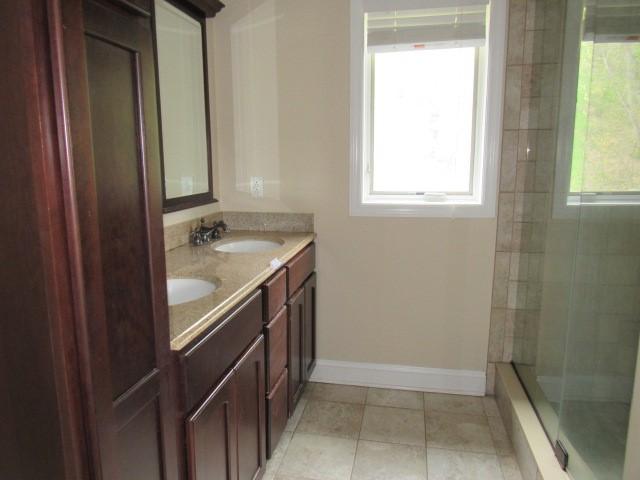 full bathroom with a sink, tiled shower, tile patterned floors, double vanity, and baseboards