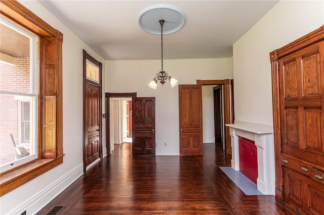 unfurnished living room featuring dark wood-style flooring, a chandelier, visible vents, and baseboards