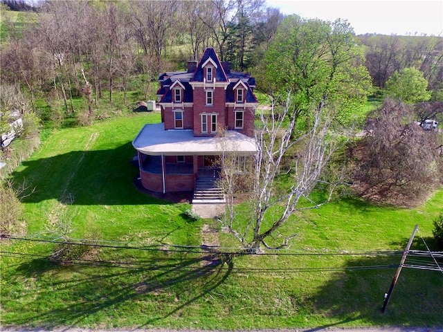 exterior space featuring a porch, a front lawn, stairway, brick siding, and a wooded view
