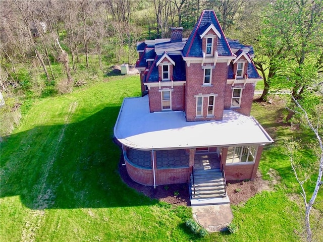 view of front facade with a chimney, covered porch, brick siding, stairway, and a front lawn