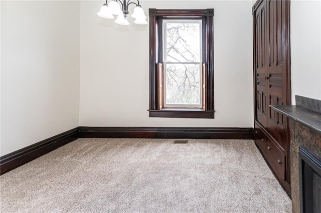 carpeted spare room with visible vents, a notable chandelier, and baseboards