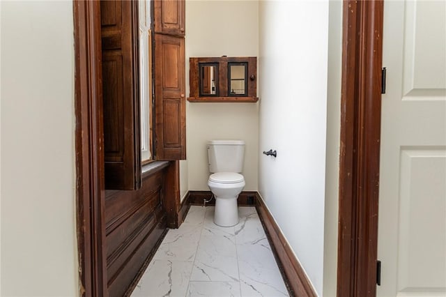 bathroom with toilet, marble finish floor, and baseboards