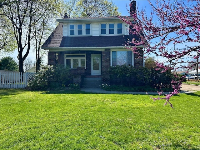 view of front of property with fence, a chimney, a front yard, and brick siding