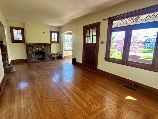 unfurnished living room with arched walkways, hardwood / wood-style flooring, a fireplace with raised hearth, baseboards, and visible vents