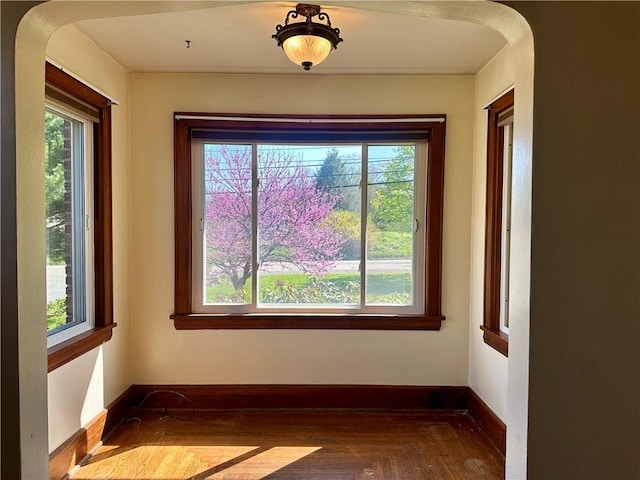 unfurnished room featuring arched walkways, a wealth of natural light, wood finished floors, and baseboards