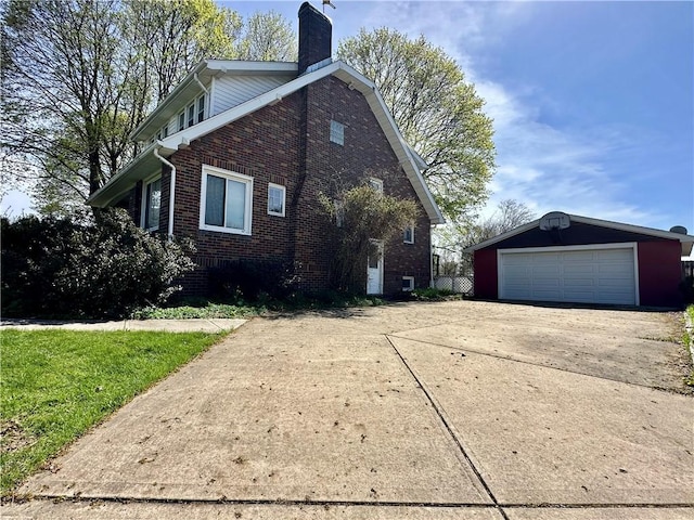 view of home's exterior featuring an outbuilding, a detached garage, a chimney, and brick siding