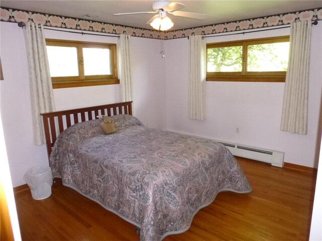 bedroom featuring baseboards, wood finished floors, a baseboard heating unit, and multiple windows