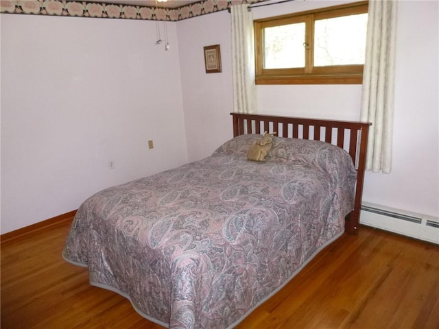 bedroom with wood finished floors and a baseboard radiator