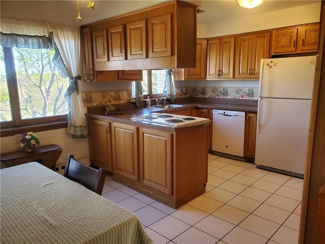 kitchen with a sink, brown cabinets, a peninsula, white appliances, and dark countertops