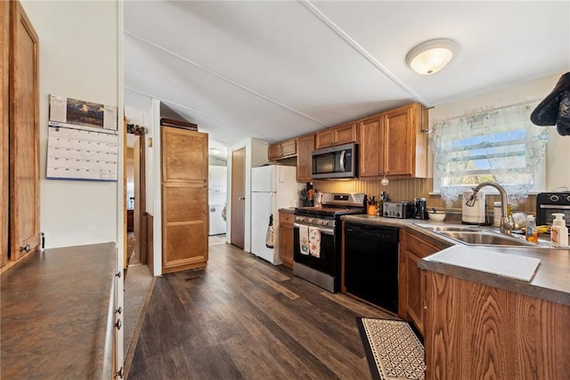 kitchen with brown cabinets, a sink, dark wood-style flooring, stacked washer and dryer, and appliances with stainless steel finishes