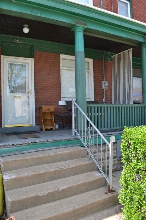 view of exterior entry featuring covered porch and brick siding