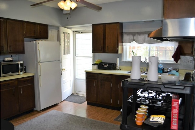 kitchen featuring stainless steel microwave, ceiling fan, light countertops, freestanding refrigerator, and wall chimney exhaust hood
