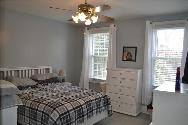 bedroom featuring a ceiling fan, light carpet, and multiple windows