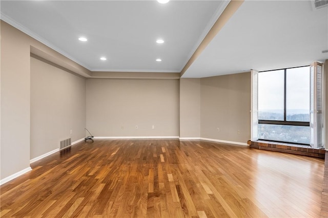 unfurnished room featuring baseboards, visible vents, ornamental molding, and wood finished floors