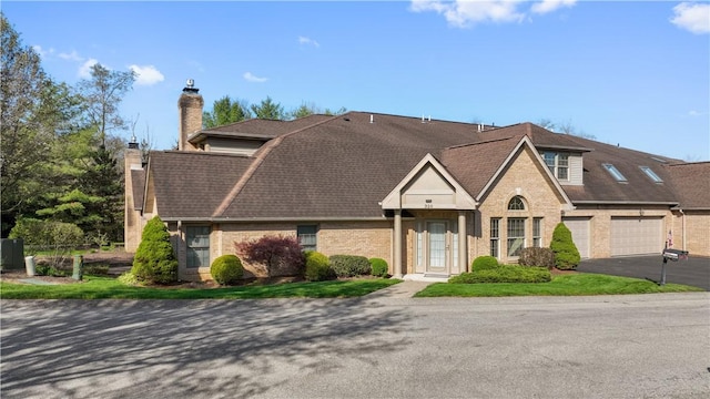 view of front of house featuring a chimney, brick siding, driveway, and roof with shingles