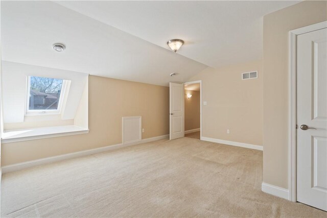 empty room featuring baseboards, visible vents, light colored carpet, and vaulted ceiling