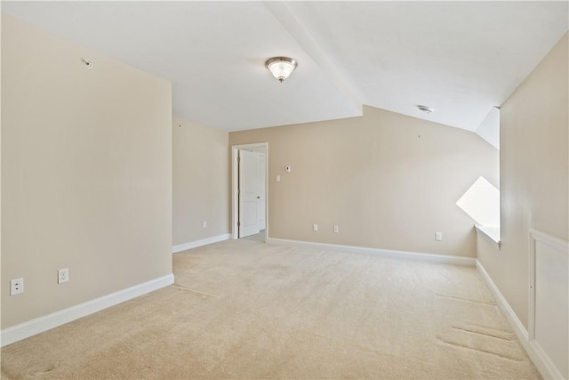 empty room featuring lofted ceiling, light carpet, and baseboards