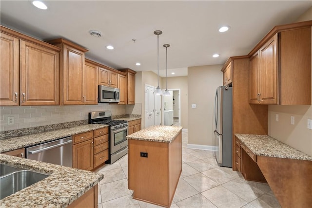 kitchen with brown cabinets, tasteful backsplash, appliances with stainless steel finishes, a center island, and light stone countertops