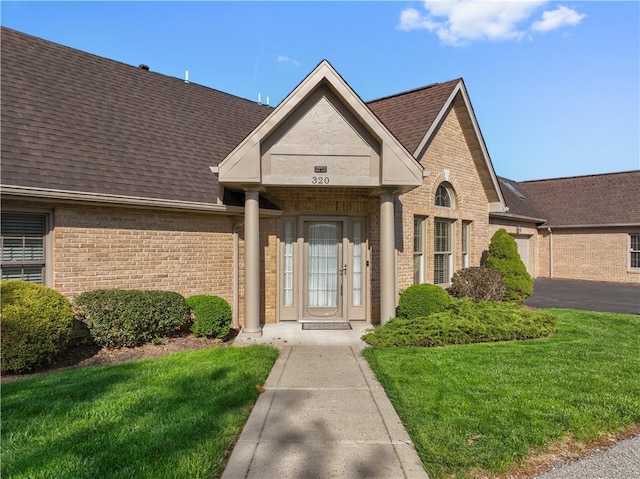 view of front facade featuring roof with shingles, a front lawn, and brick siding