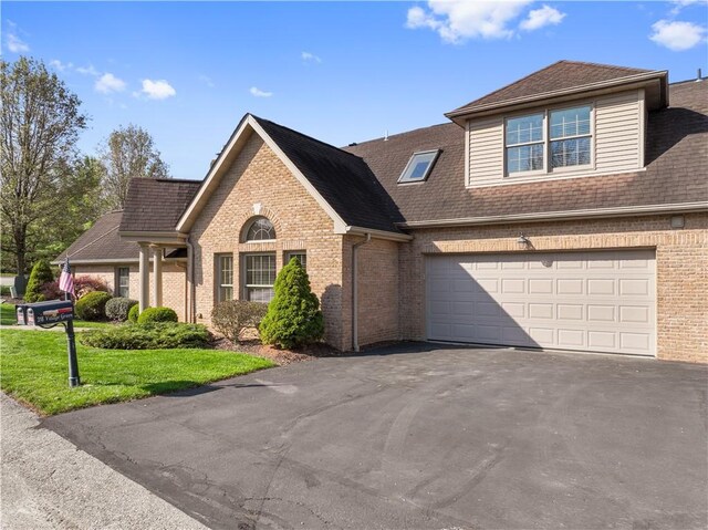 traditional-style home featuring roof with shingles, a front lawn, aphalt driveway, and brick siding