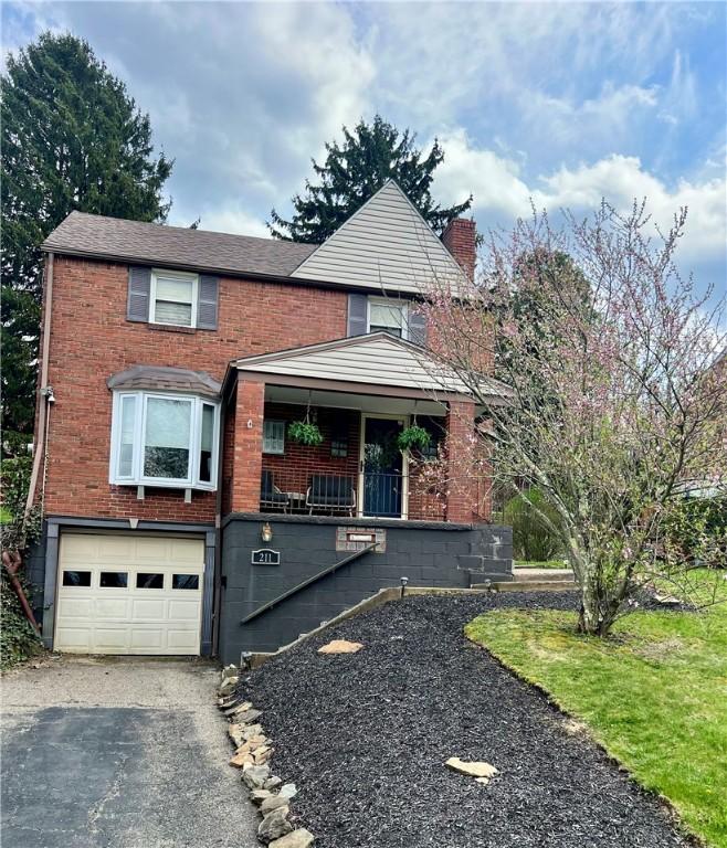 211 Constitution Ave, West Mifflin, PA 15122 - traditional home with aphalt driveway, covered porch, stairway, brick siding, and a garage