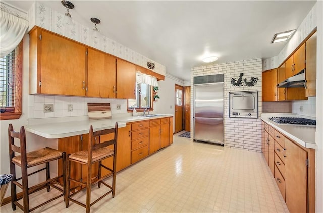 kitchen with a sink, light countertops, stainless steel appliances, under cabinet range hood, and visible vents
