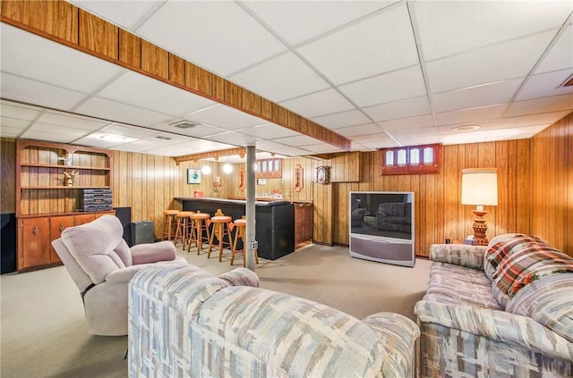 carpeted living room with a bar, wood walls, and a paneled ceiling