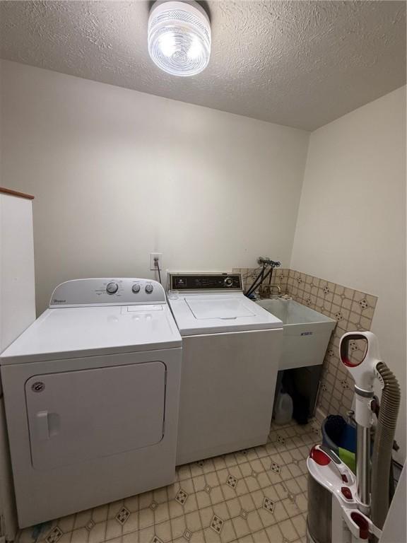 washroom featuring laundry area, a textured ceiling, washing machine and clothes dryer, a sink, and light floors